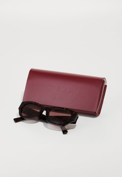 Étui à lunettes Gucci bordeaux avec logo embossé. Lunettes rectangulaires en écaille de tortue foncée avec des montures épaisses et des branches élégantes.