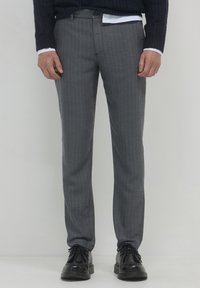 Pantaloni grigi a motivo spina di pesce con vestibilità dritta, dotati di chiusura a bottone e tasche frontali, abbinati a scarpe nere stringate.