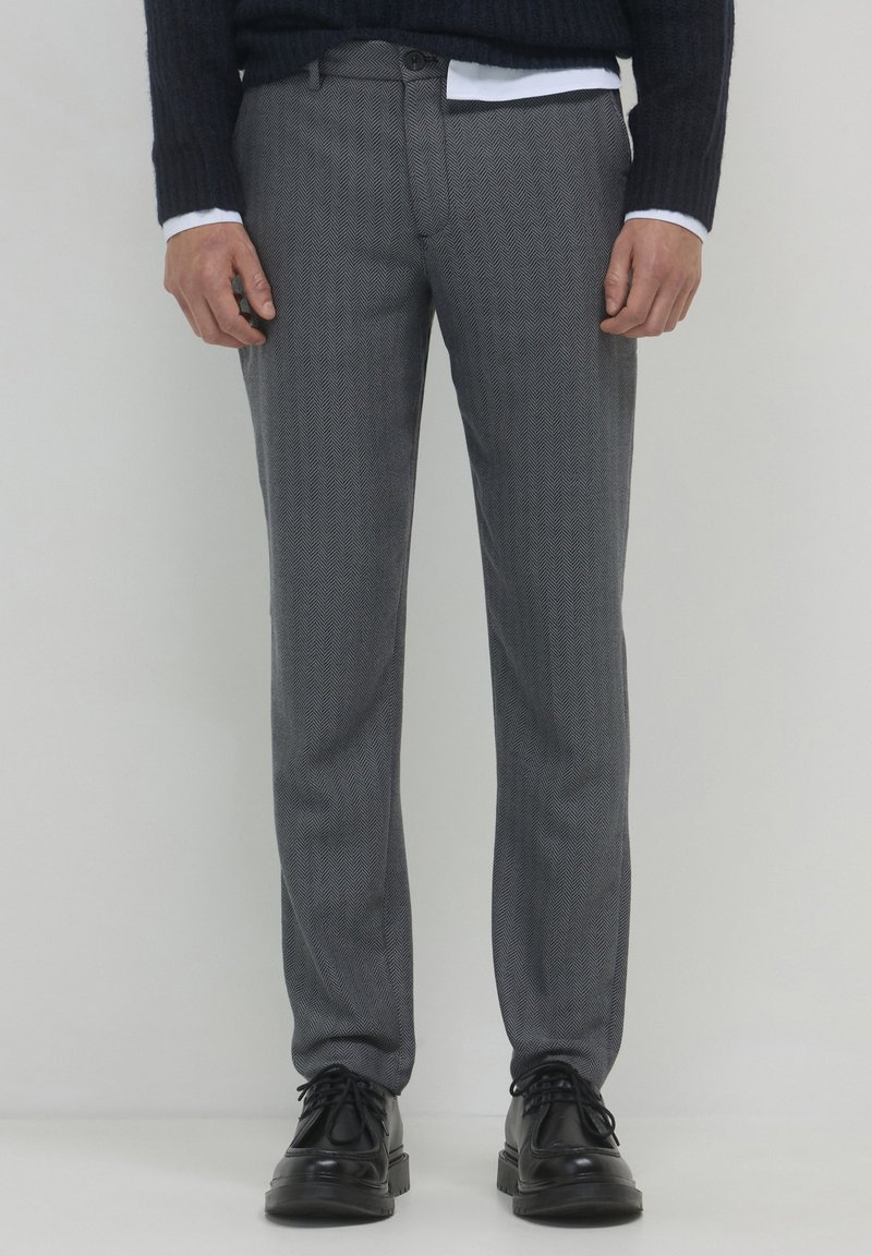 Pantaloni grigi a motivo spina di pesce con vestibilità dritta, dotati di chiusura a bottone e tasche frontali, abbinati a scarpe nere stringate.