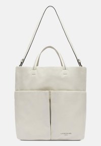 Hellebeige Lederhandtasche mit doppelten Griffen und einem langen, verstellbaren Schulterriemen. Sie verfügt über eine Frontreißverschlusstasche und das Markenlogo, das am Boden angebracht ist.