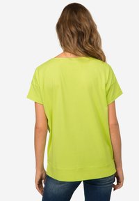 Limoengroene T-shirt met korte mouwen, ontspannen pasvorm, ronde halslijn en zijsplitdetails, gecombineerd met blauwe denim jeans.