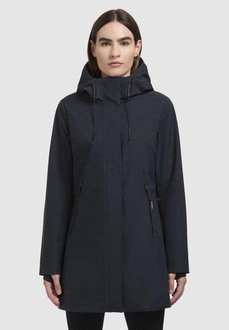 Marinblå vattentät jacka med huva, långa ärmar och fickor med dragkedja. Har en elegant, slät textur och minimalistisk design.