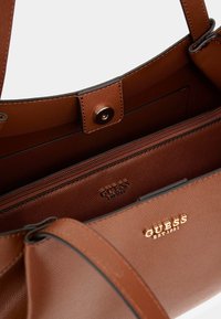Braune, strukturierten Lederhandtasche mit goldenen Hardware-Akzenten, ausgestattet mit einem Reißverschluss-Innenfach und geprägtem Markenlogo im Inneren.