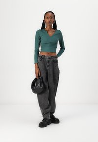Grønn ribbet langermet crop top, høyt liv svarte baggy jeans, svart håndveske og chunky svarte sko. Minimalistisk design med moderne detaljer.