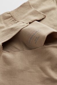 Lysebrun stof har en blød tekstur med en foldet krave og et synligt mærke med brandnavn og størrelse indeni plagget.