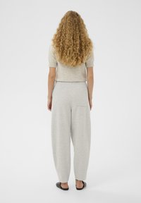 Rövidujjú, világosszürke felső bordázott mandzsettával, laza, világosszürke melegítőnadrággal, amelyen hátsó zseb található, és fekete lapos szandál.