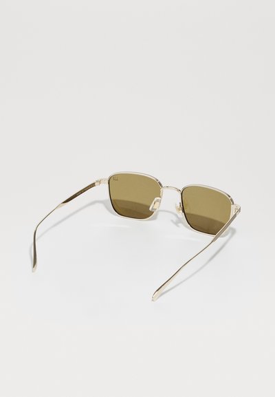 Lunettes de soleil rectangulaires avec une fine monture en métal doré et des verres teintés marron. Les branches présentent des détails texturés subtils pour une meilleure prise.