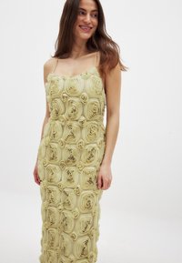 Robe jaune clair avec des bretelles spaghetti, présentant un design texturé de roses en tissu. La robe a une silhouette ajustée et tombe jusqu'au sol.