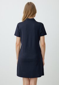 Korte mouwen, marineblauwe polokleid met een rechte pasvorm, zachte stof en een kraag. Eindigt boven de knie met een gladde textuur. Geen opmerkelijke patronen.