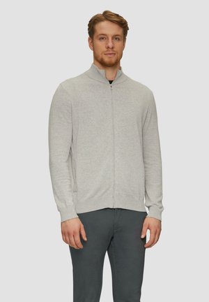 Pull zippé gris clair avec col montant, poignets et ourlet côtelés, et texture lisse, associé à un pantalon foncé.