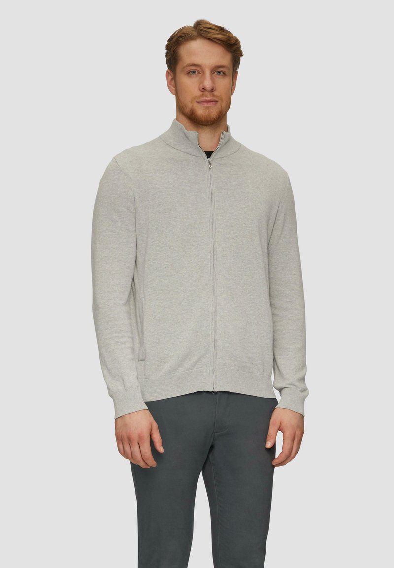 Hellgrau zip-up Sweater mit Stehkragen, gerippten Bündchen und Saum sowie glatter Textur, kombiniert mit schwarzen Hosen.