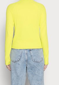 Long-sleeve, ribbed top in bright yellow, paired with light blue, high-waisted denim jeans. Simple design with no visible patterns or accents.