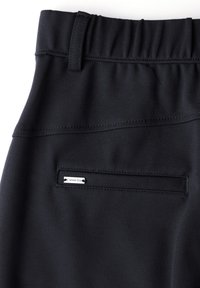 Černé elastické kalhoty s nařaseným pasem. Mají zabezpečenou zadní kapsu a malou kovovou logo nášivku. Hladká textilie.
