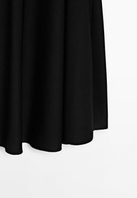 Sorte stofgardin hængende med bløde folder og rene kanter mod en hvid baggrund.