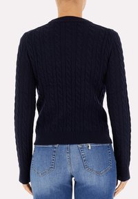Maglione navale a trecce con maniche lunghe, colletto e orlo a coste, motivo testurizzato, abbinato a jeans blu aderenti visibili sotto.