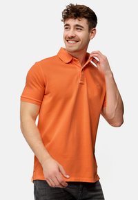 Oranje poloshirt van katoen met korte mouwen, een kraag en een klein logo op de borst. Draag het met een donkere spijkerbroek.
