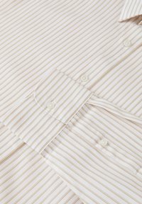 Camicia bianca con sottili righe beige, dotata di un'impostazione frontale con bottoni e collo. Tessuto strutturato con una finitura liscia.