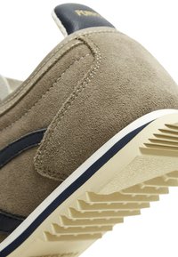 Suede tenisice u taupe boji s mornarskom akcentom, s teksturiranom potplatom, kontrastnim bijelim prugama i detaljno šivenjem blizu pete.