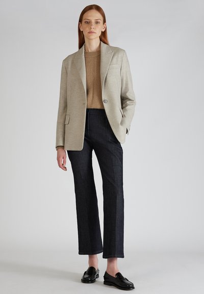 Blazer grigio chiaro sopra un maglione beige, jeans scuri e mocassini neri. Il blazer presenta revers a punta, bottone singolo e tasche frontali.