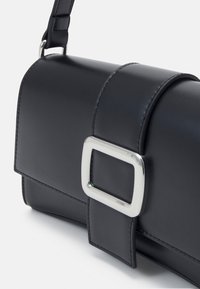 Czarna skórzana torba na ramię z dużą, srebrną, prostokątną klamrą na przedniej klapie, prezentowana na jednolitym białym tle.