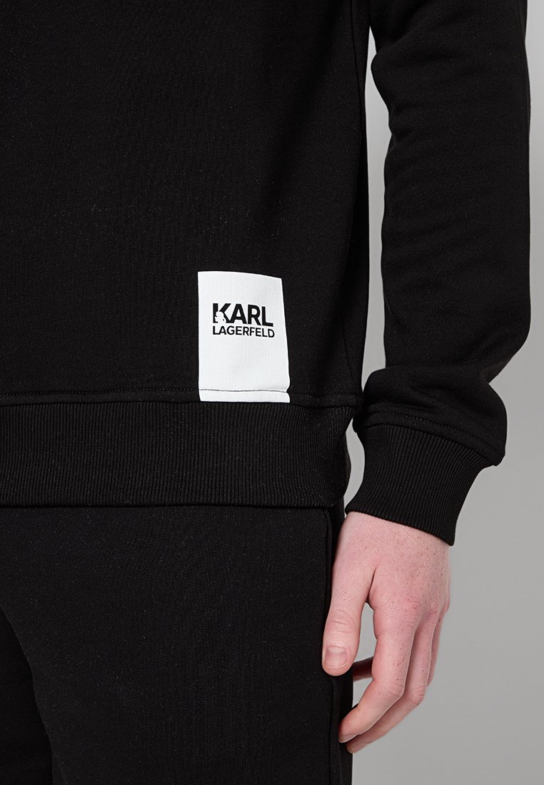 Schwarzer Hoodie mit gerippten Bündchen und Saum, ausgestattet mit einem weißen Logo-Patch mit der Aufschrift "KARL LAGERFELD" auf der unteren Vorderseite. Aus weichem Baumwollstoff.