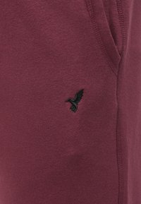 Ύφασμα φούτερ σε μπορντό με μαλακή υφή, που διαθέτει μαύρο κεντημένο λογότυπο πουλιού στην αριστερή πλευρά. Περιλαμβάνει πλευρικές τσέπες.