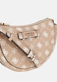 Beige Guess monogram crossover taske med justerbar rem, guld lynlås og guld logo-plade med indgraveringen "GUESS EST 1981."