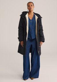 Zwarte parka met voering van bont, knoopsluiting denim top en wijde denim broeken. Beschikt over een capuchon, ritsluiting en grote voorzakken.