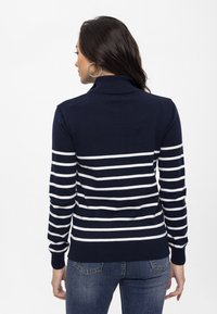 Pull bleu marine avec des rayures blanches horizontales, conçu en col roulé, avec des poignets et un ourlet côtelés, associé à un jean bleu.