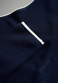 Tengerészkék kötött pulóver fehér bordázott betétekkel a nyakkivágásnál és az ujjszéleknél, texturált anyagból, hogy melegen tartson.