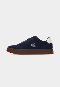 Baskets basses bleu marine avec détail blanc au talon, semelle marron, lacets noirs et logo blanc "cK" sur le côté.