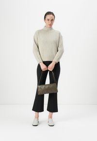 Borsa a tracolla khaki trapuntata con manico corto, appoggiata contro un maglione chiaro e pantaloni neri. Texture morbida e a coste, forma rettangolare.