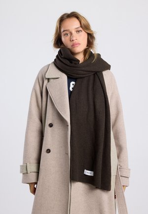 Donkerbruine sjaal van zachte stof, draped om de nek, gecombineerd met een lichtbeige jas met een getailleerd ontwerp en knopen.