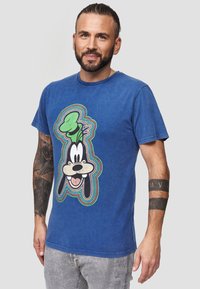 Blauwe katoenen T-shirt met een afbeelding van een cartoonfiguur met een groene hoed. Korte mouwen en een ronde halslijn. Versleten textuur.