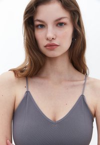 Top gris de cuello en V con tirantes finos, que presenta un patrón texturizado y acanalado. La tela tiene un acabado suave y un diseño ajustado.