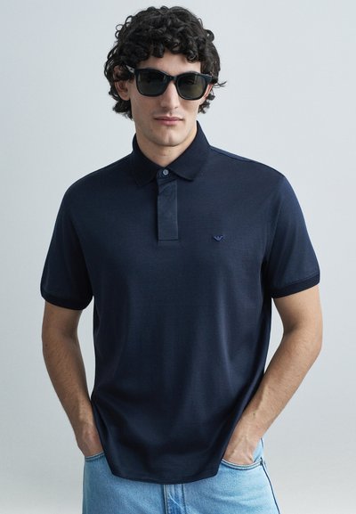 Marineblauw poloshirt van een zachte stof met een knoopsluiting en korte mouwen; heeft een klein logo op de borst en een comfortabele pasvorm.
