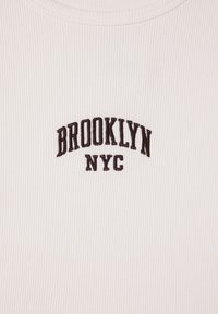 Biała koszulka T-shirt z żebrowanej tkaniny z czarnym haftowanym napisem "BROOKLYN NYC" w zakrzywionym wzorze na przodzie.