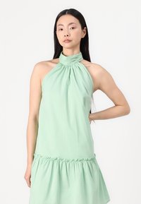 Mint zelena obleka s halter vratom, z nabranim zgornjim delom in nabranim robom, izdelana iz lahkega materiala. Gladka tekstura in preprost dizajn.