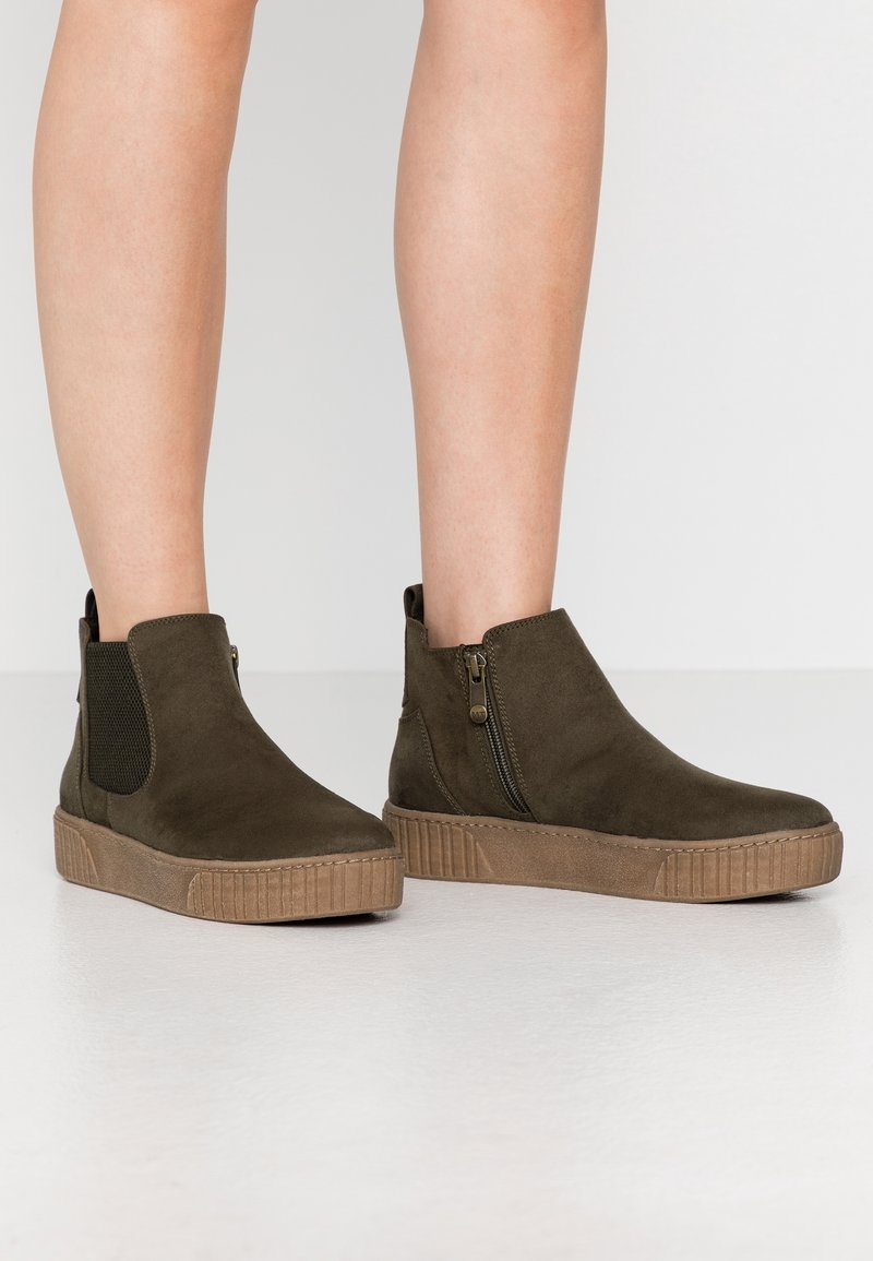 Olivgröna ankelskängor i mocka, med elastiska sidopaneler, en sidodragkedja och en strukturerad sula. Formen är kort med en rund tå.