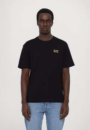 Melna kokvilnas T-krekls ar zelta EA7 logotipu kreisajā krūšu daļā, īsām piedurknēm un klasisku apaļu kakla dizainu.