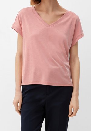 Roze T-shirt met korte mouwen en V-hals, gemaakt van een zachte, gestructureerde stof. Relaxte pasvorm met iets opgerolde mouwboorden. Draagt bij donkere broek.