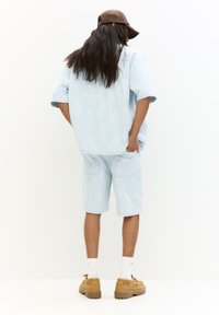 Světle modrý džínový outfit, který zahrnuje tričko s krátkým rukávem a šortky ke kolenům, oba zdobené bílou květinovou výšivkou a náprsními kapsami.