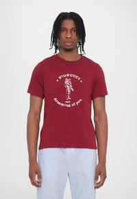 Burgundy cotton t-shirt featuring a white graphic print with "Fiorucci" and "dreaming of you," alongside vertical striped pants.