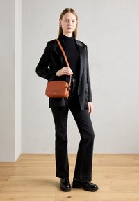 Black wool blazer over a black turtleneck, paired with flared black jeans and black platform shoes. Holding a brown leather crossbody bag.