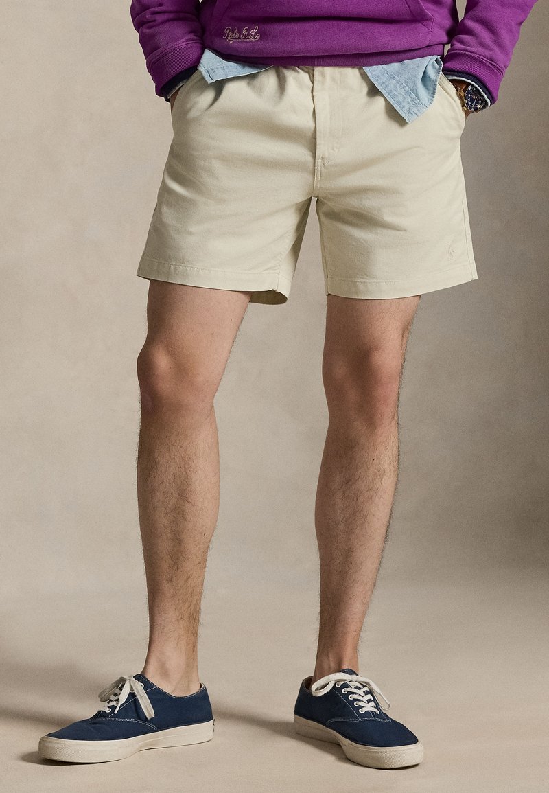 Khaki shorts in a lightweight cotton fabric with a relaxed fit. Paired with navy canvas sneakers featuring white laces and a rubber sole.