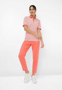 Polo a righe in corallo e bianco, maniche corte, colletto con bottoni; abbinato a pantaloni corallo e sneakers bianche.
