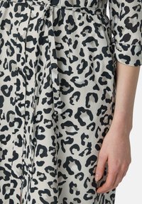 Sukienka w leopardzi wzór z lekkiego materiału, z czarnymi plamami na beżowym tle, z guzikami i związanym w talii detalem.