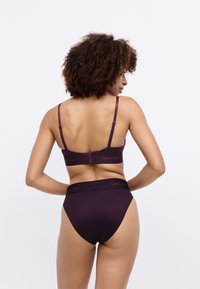 Lila alsónemű szett, amely tartalmaz egy varrat nélküli melltartót állítható pántokkal és egy hozzá illő, magas derekú bugyit, mindkettő Calvin Klein márkajelzéssel.