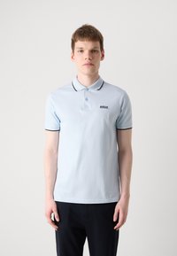 Tricou polo de culoare albastră deschisă, cu guler clasic, mâneci scurte și detalii negre în contrast. Prezintă un mic logo pe partea stângă a pieptului.