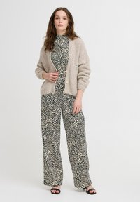 Cárdigan beige y esponjoso con botones frontales sobre un mono de estampado de cebras en blanco y negro, con piernas anchas y un escote ajustado.